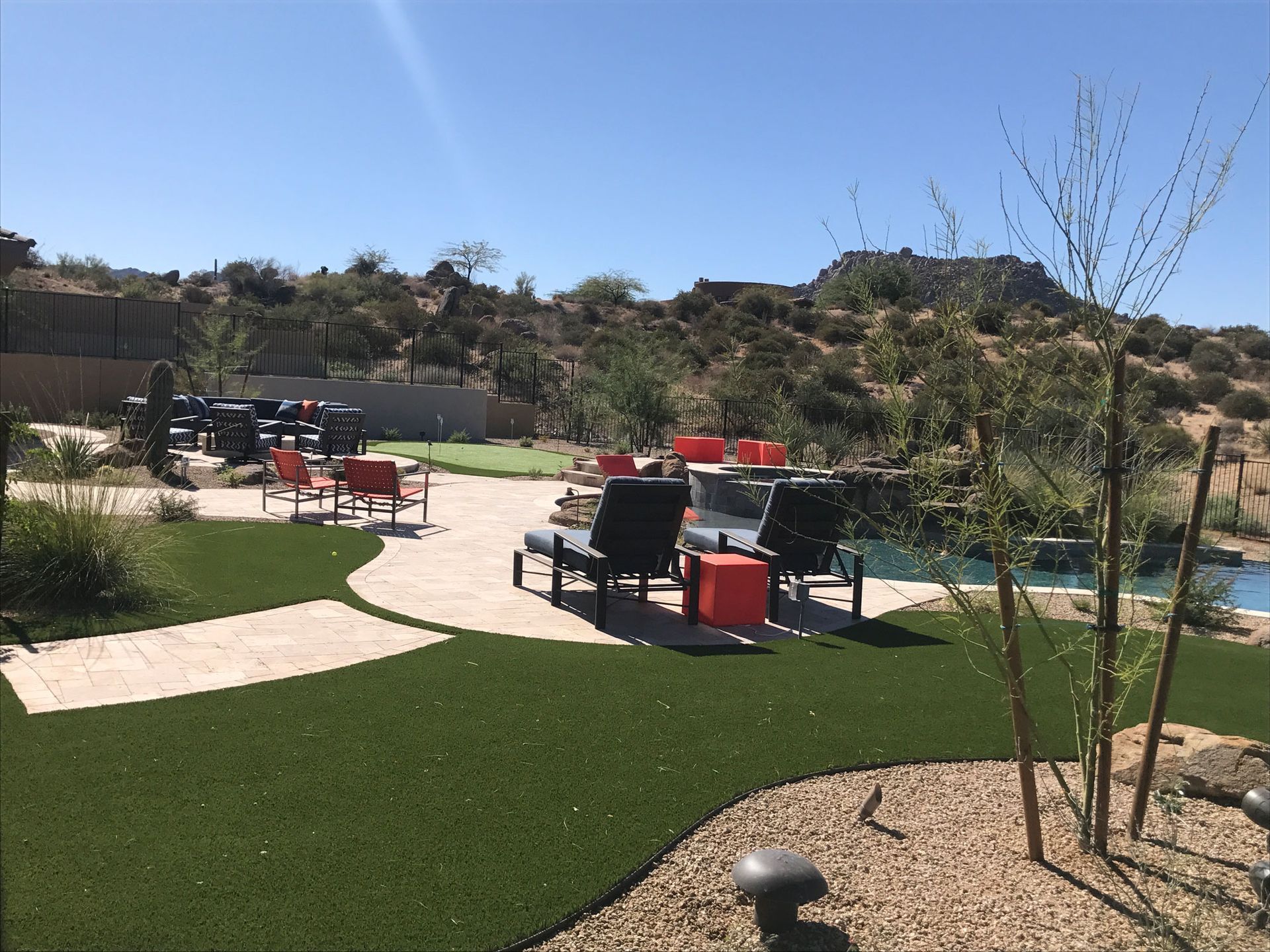 Outdoor patio with red tables, chairs, and a pool beside a grassy yard and desert hills