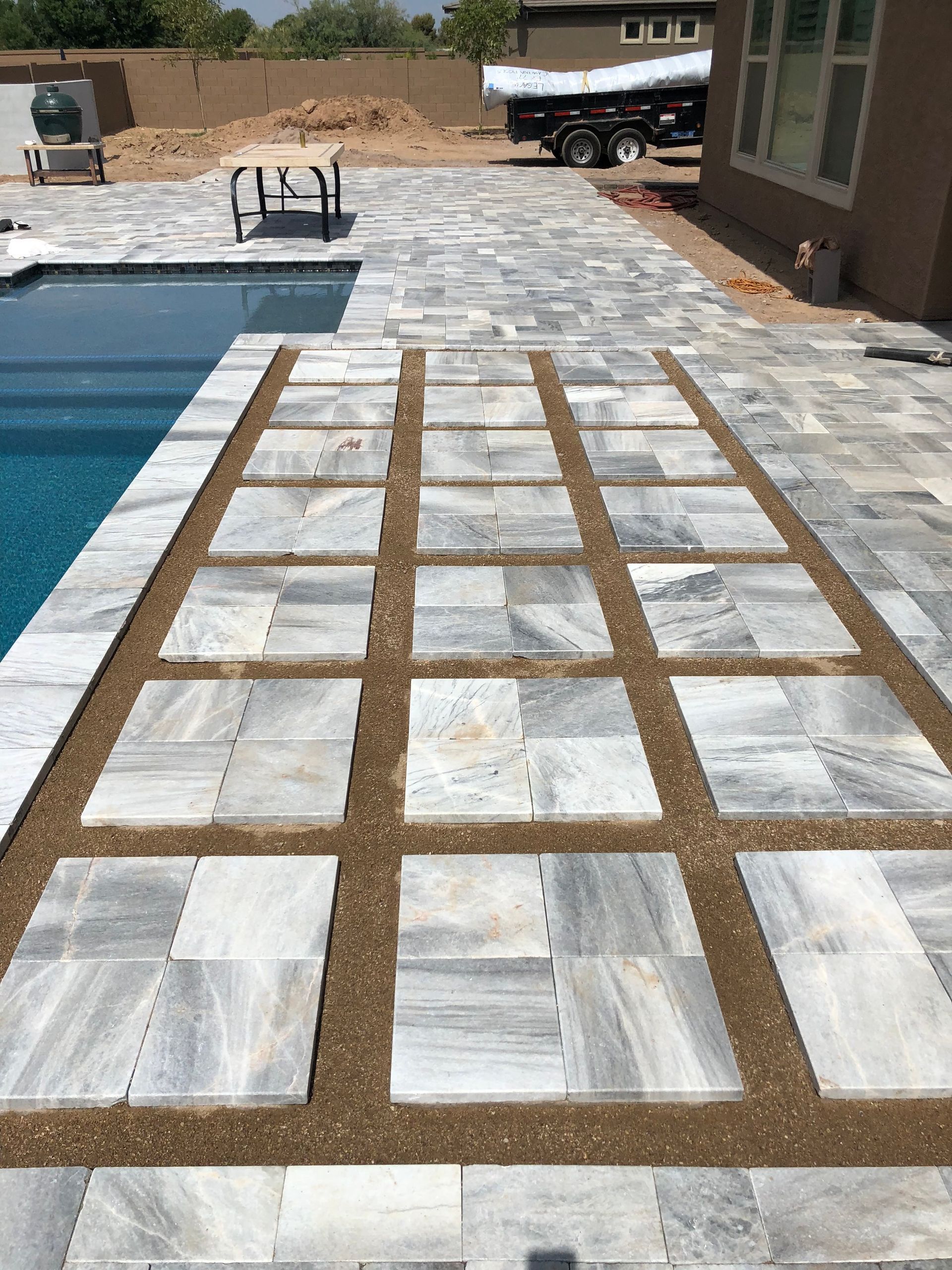 Wooden grid mold laid over stone pavers beside a swimming pool in a backyard patio.