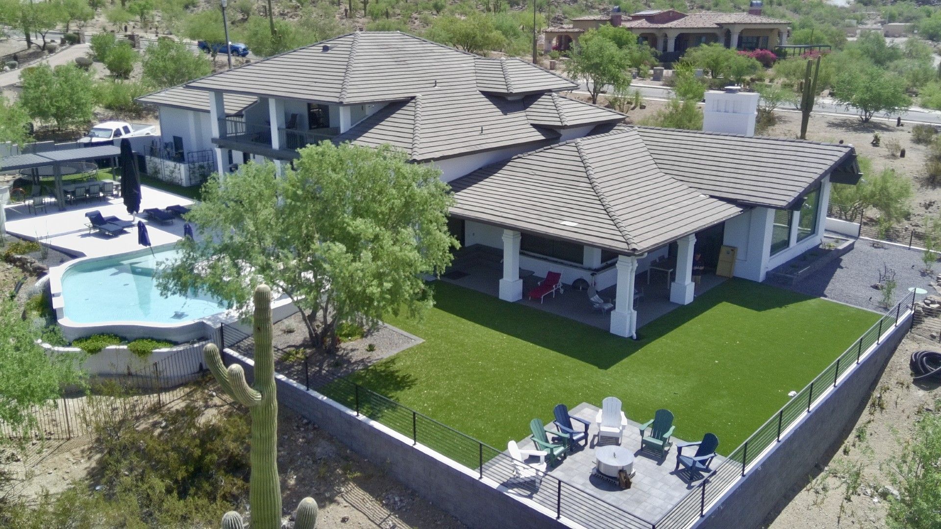 Aerial view of a modern home with a backyard pool, patio seating, and green lawn in a desert setting