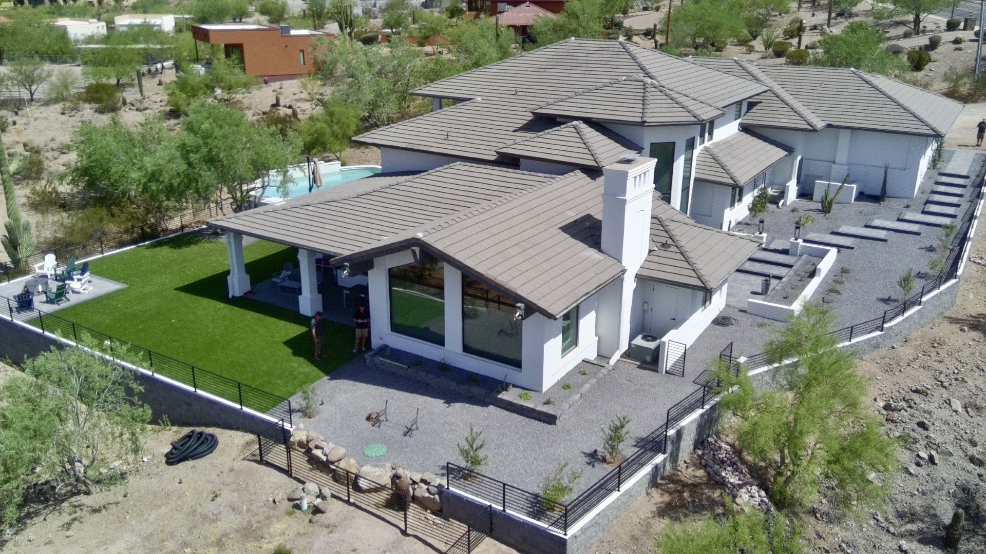 Aerial view of a large modern house with a gray roof, white pillars, and a landscaped yard in a desert setting