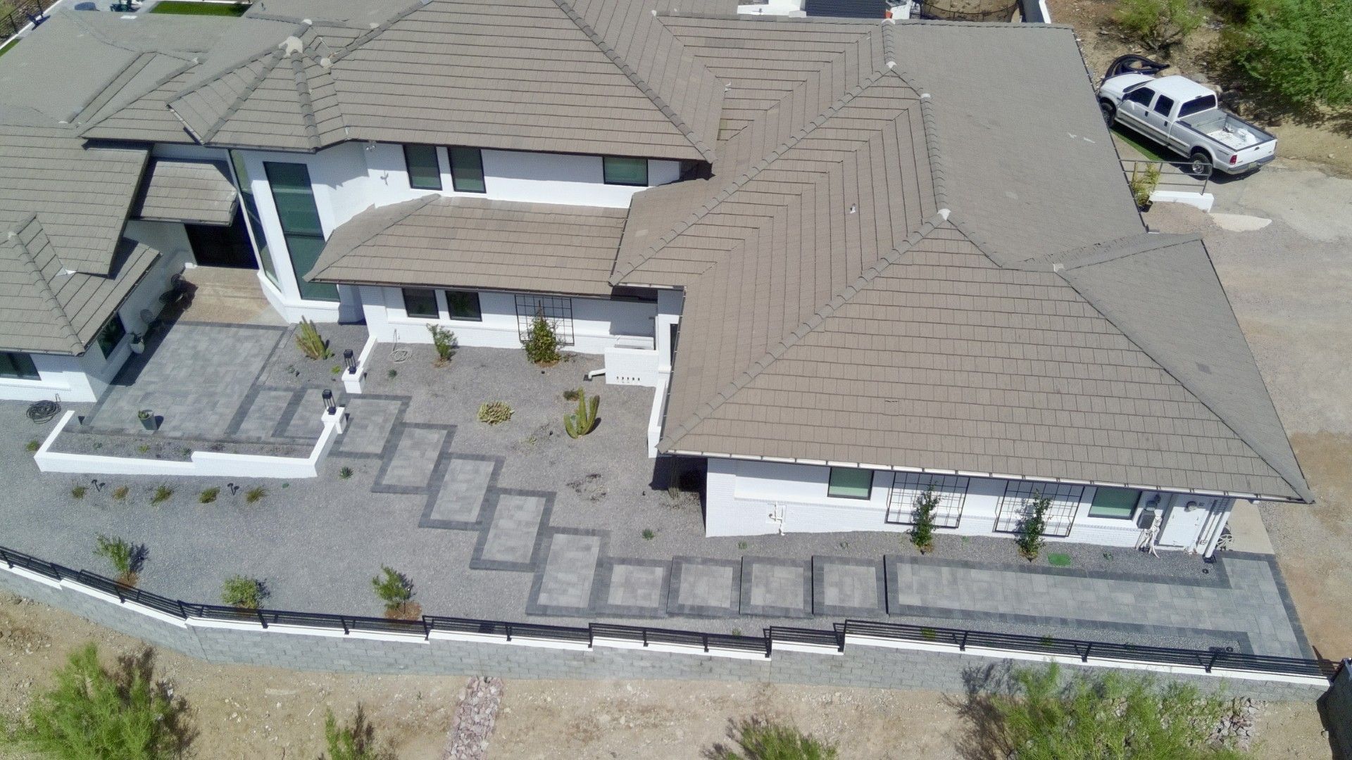 Aerial view of a modern house with a rooftop patio, stone courtyard, and surrounding driveway.