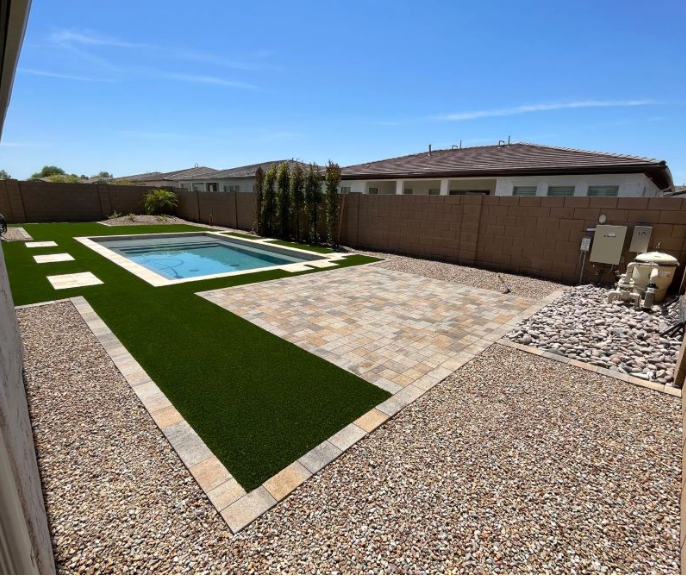 Backyard with rectangular pool, artificial turf, stone patio, and gravel landscaping under a clear blue sky