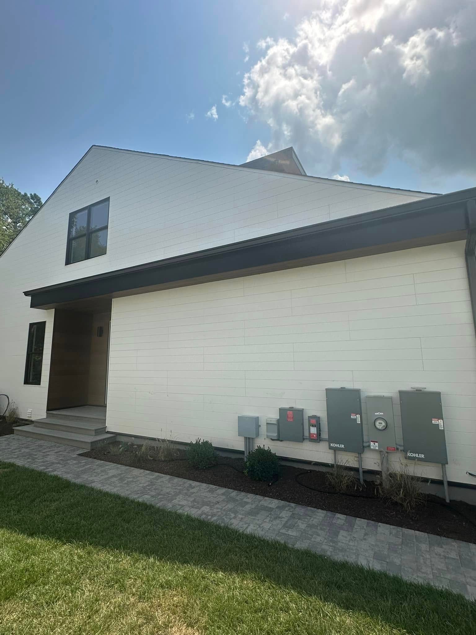 A white house with a black roof is sitting on top of a lush green lawn.