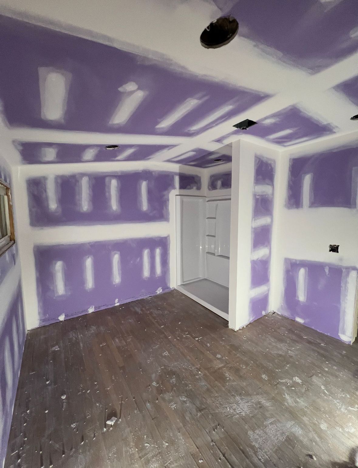 Room under construction with purple drywall, white joint compound, and a shower stall. Dark wood floor.