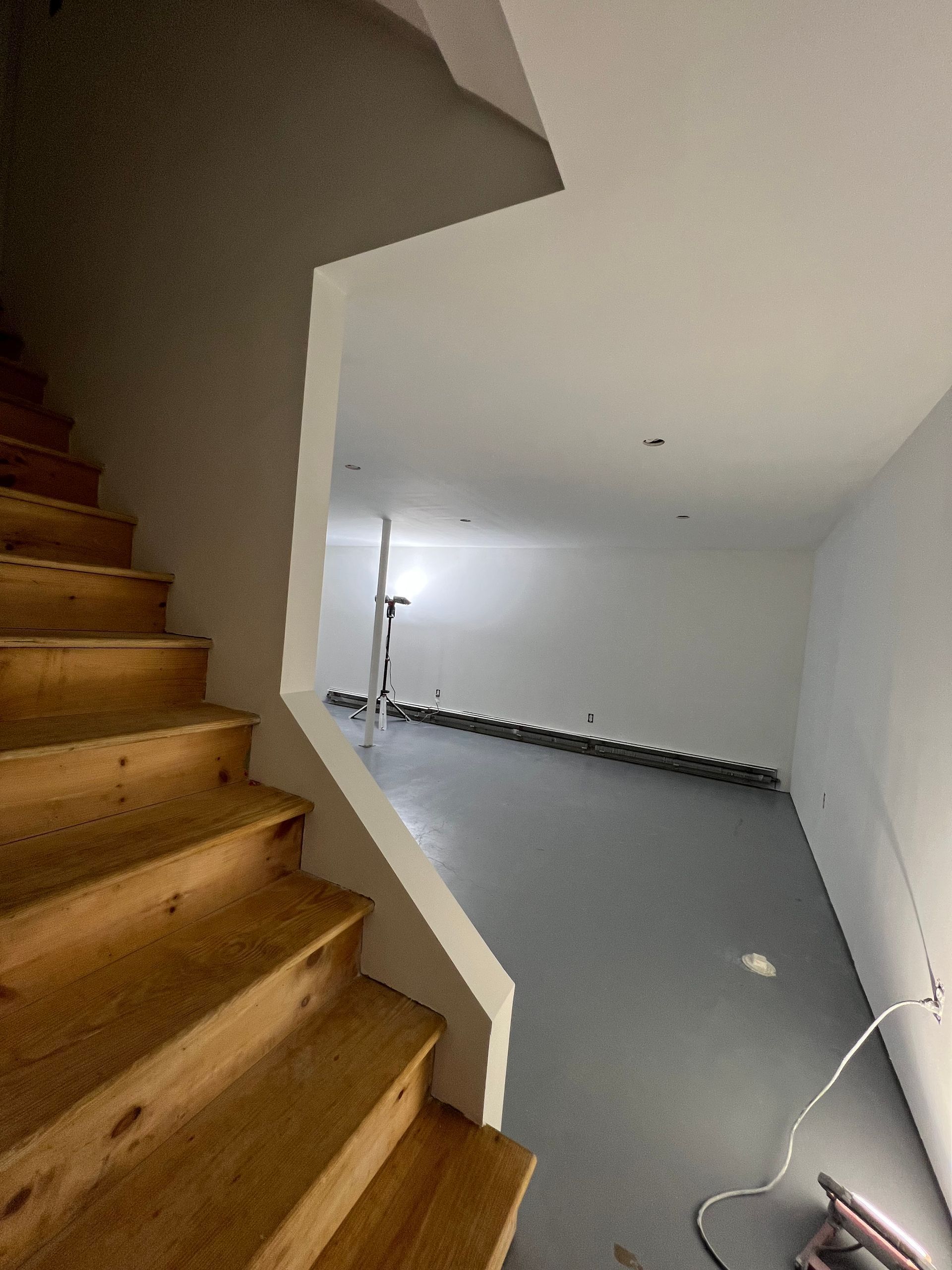 Narrow staircase beside unfinished basement room with gray floor and white walls