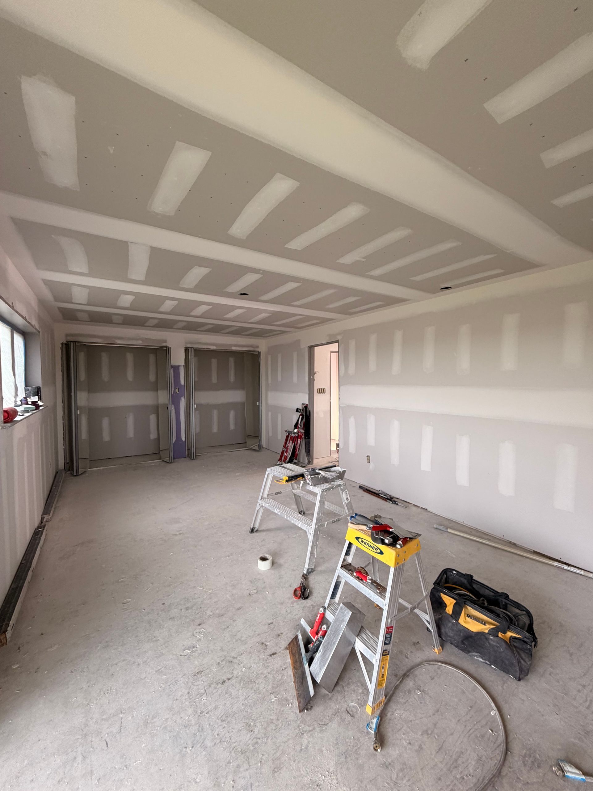 Partially finished garage with drywall seams, ladders, and tools on the floor