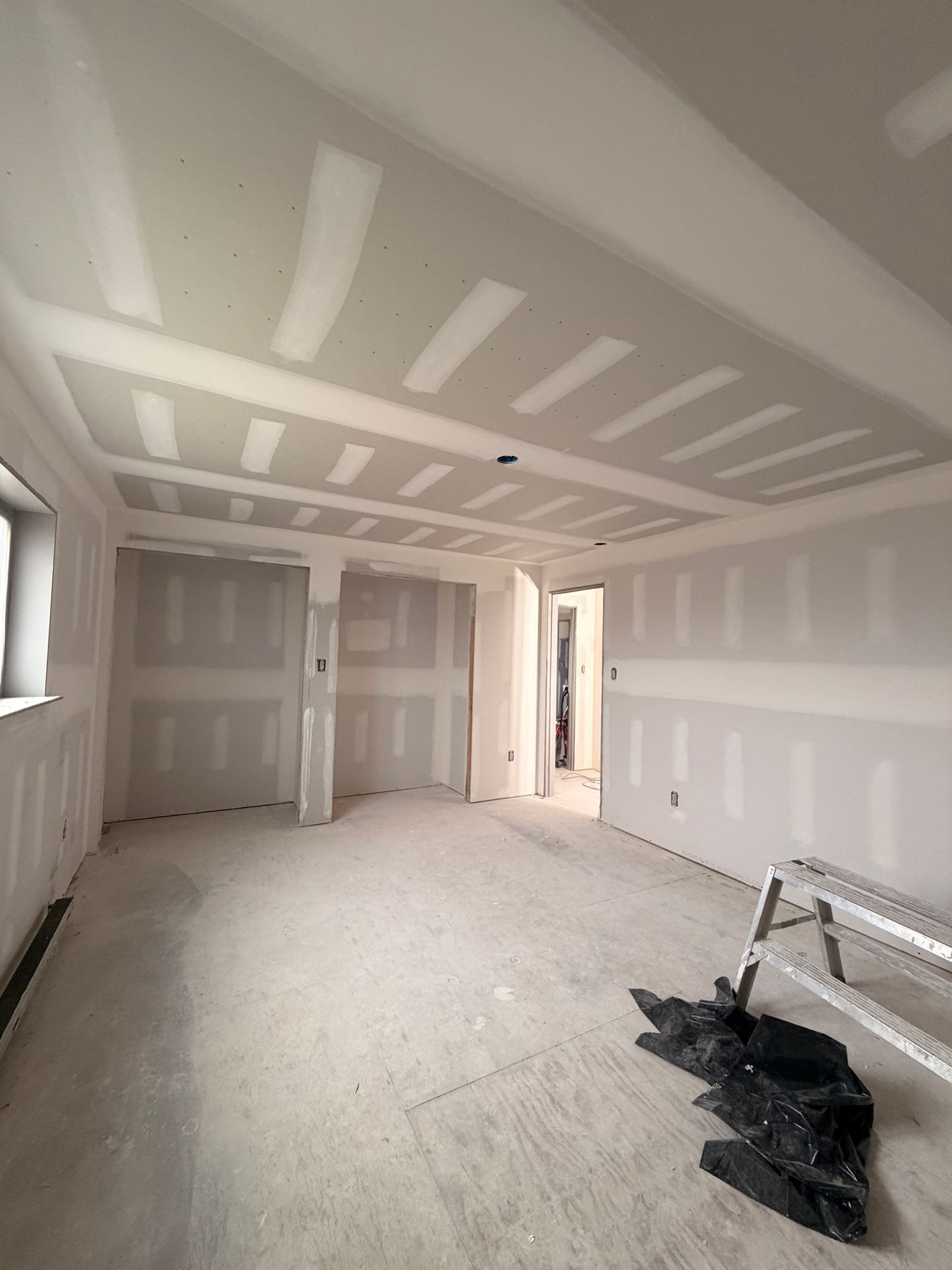Empty drywall room under construction with unfinished ceiling, taped walls, and a doorway to a lit hall