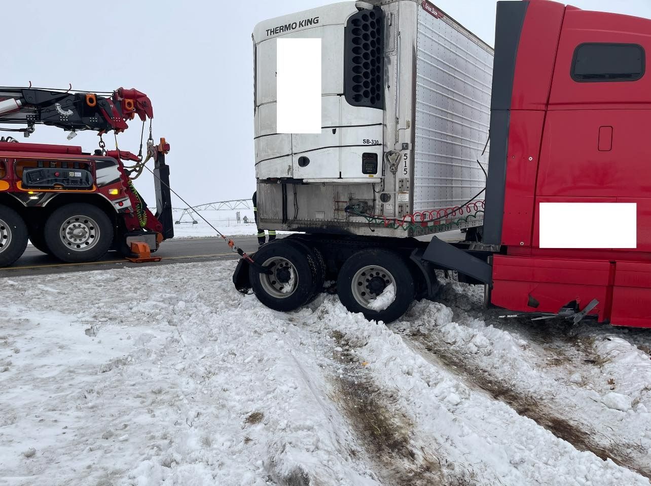 A red semi truck is being towed by a tow truck in the snow