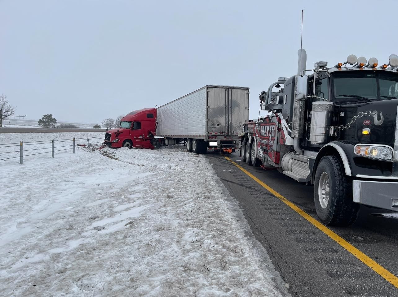 A tow truck is towing a semi-truck in the snow