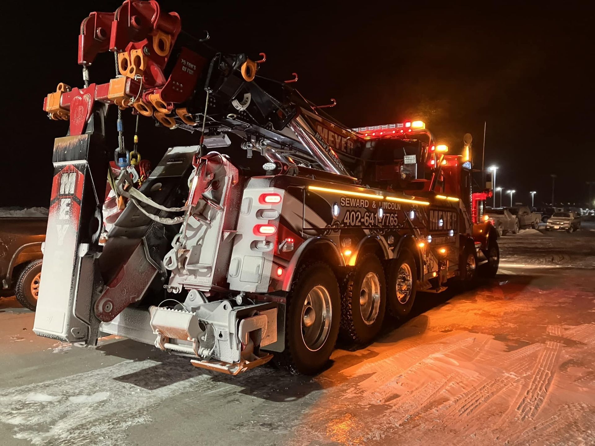 A large tow truck is parked in a parking lot at night