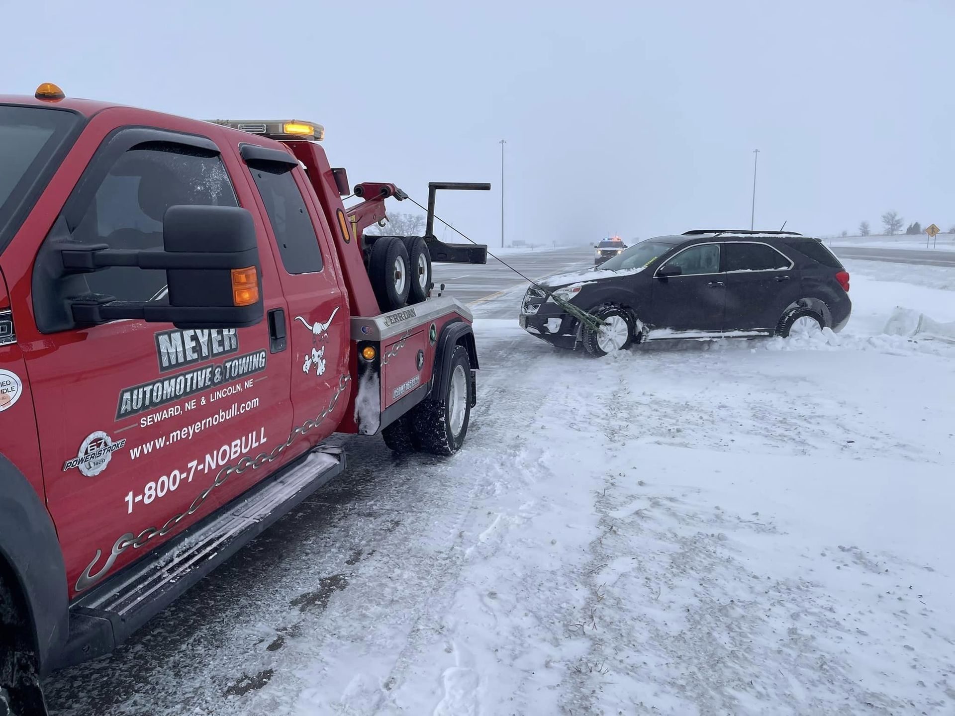 A red tow truck is towing a black suv in the snow