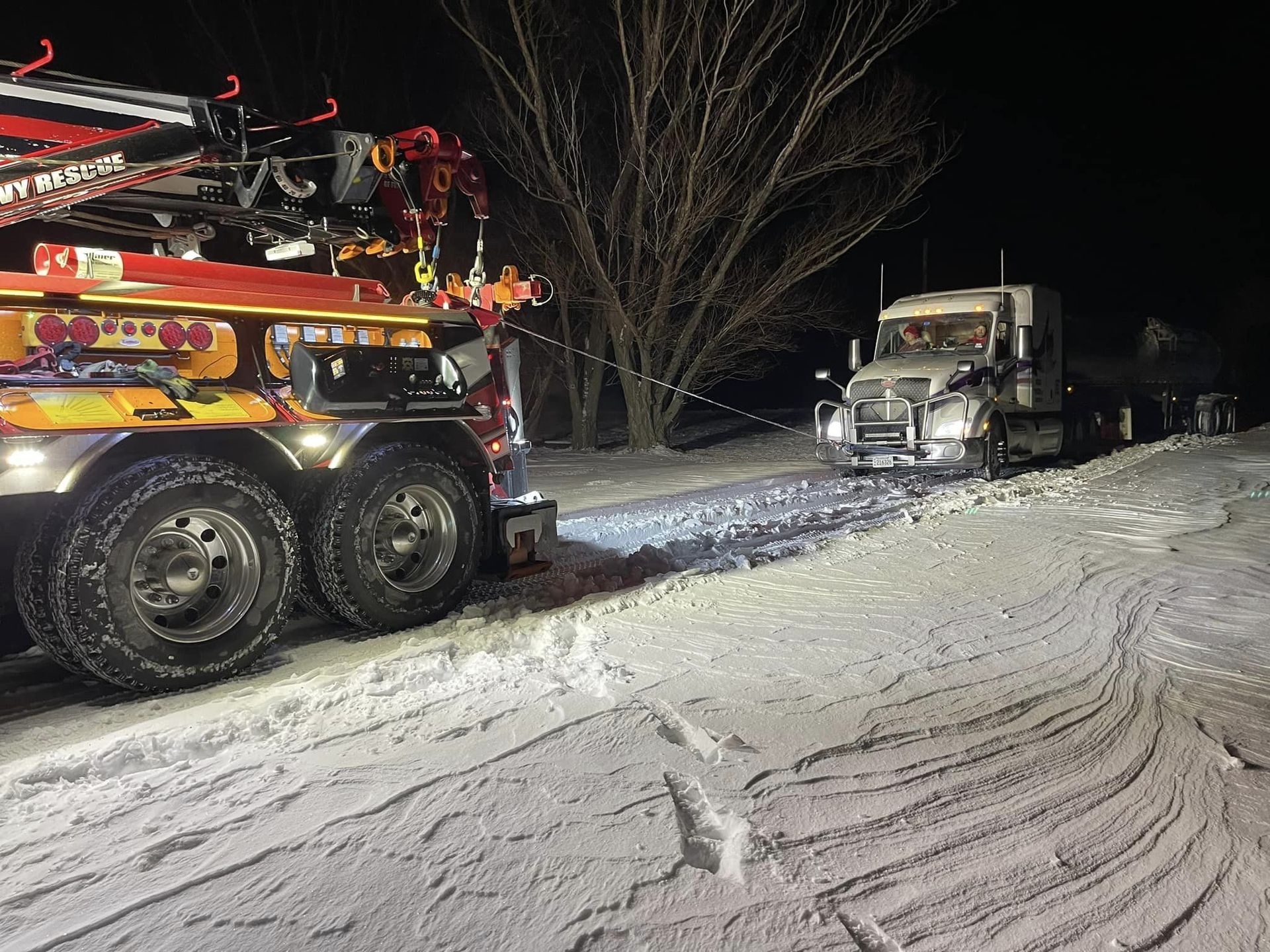 A tow truck is towing a truck in the snow at night
