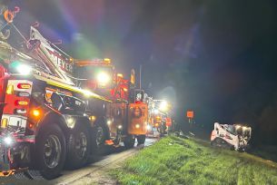 A tow truck is towing a car on the side of the road at night