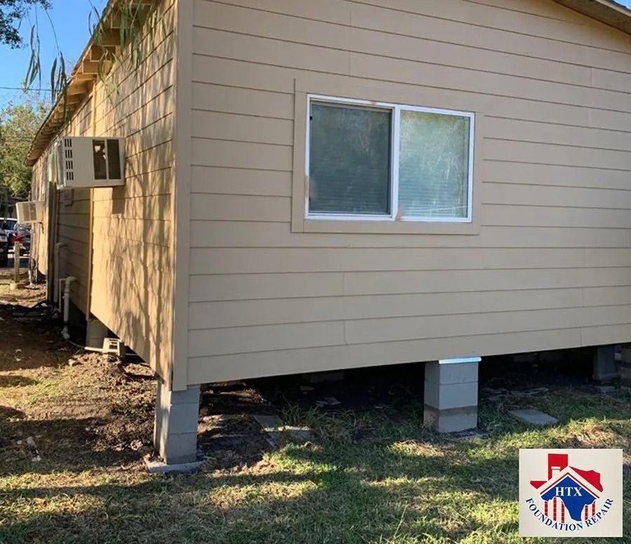 Raised beige house exterior with a window, supported on concrete blocks in a yard