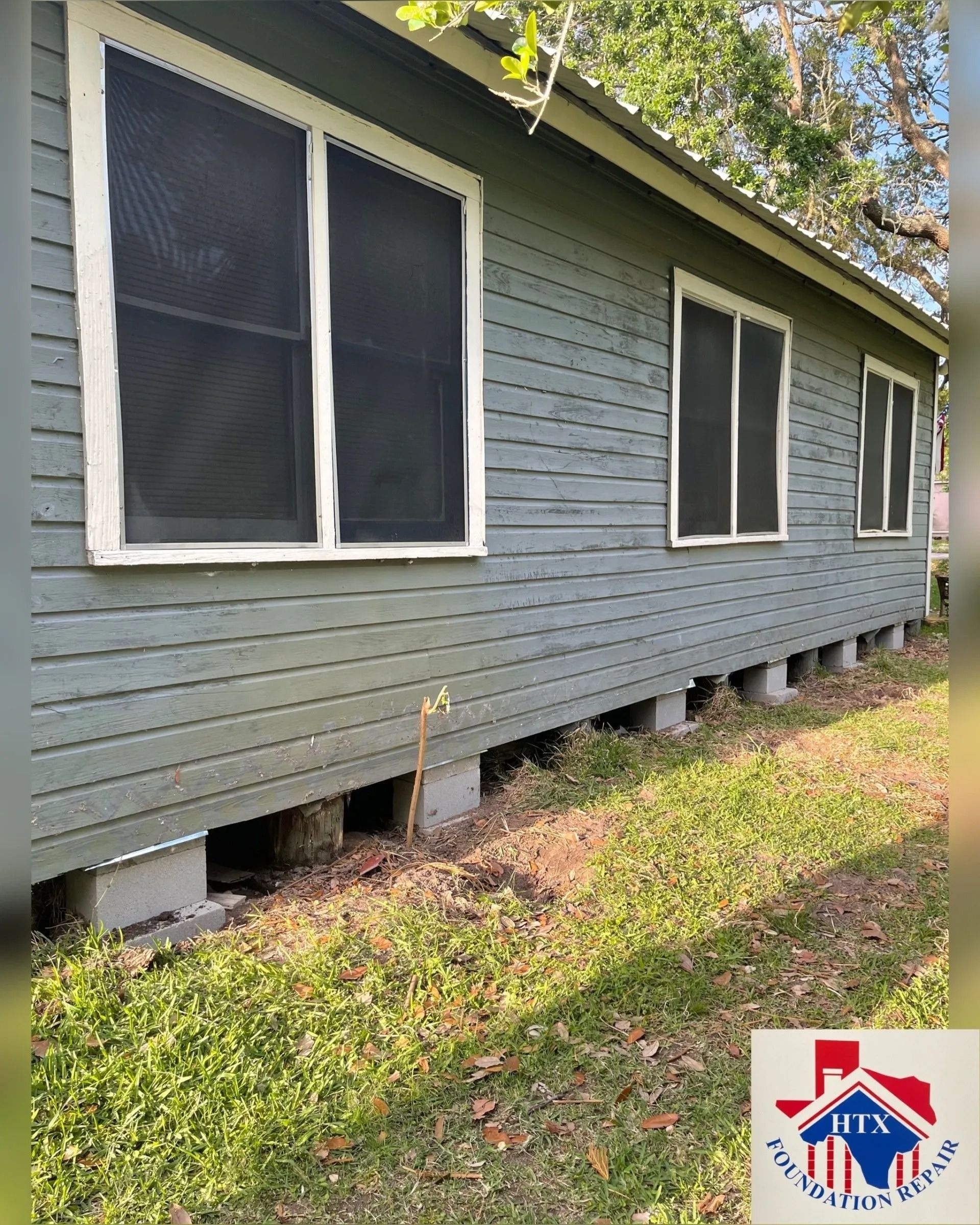 Gray house exterior with screened windows and low crawlspace openings along a grassy slope