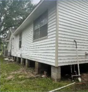 White house on raised cinder blocks with white siding and a ladder leaning against the side.