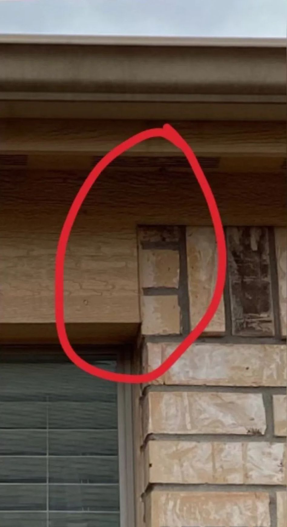 Close-up of a house exterior corner with stone wall, window, and red circle highlighting a vertical seam.
