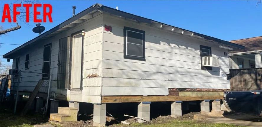 After photo of a raised white house with damaged siding under a blue sky