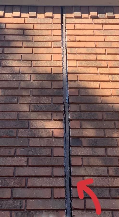 Close-up of a brick wall with a vertical seam and a red arrow pointing upward near the bottom.