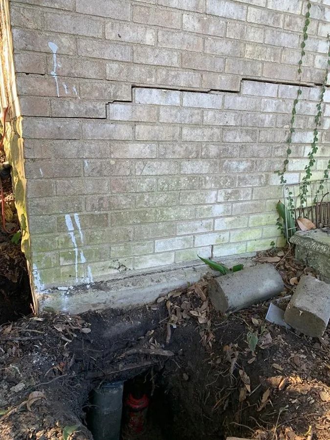 Basement wall with a dug-out excavation and exposed pipes beneath the foundation