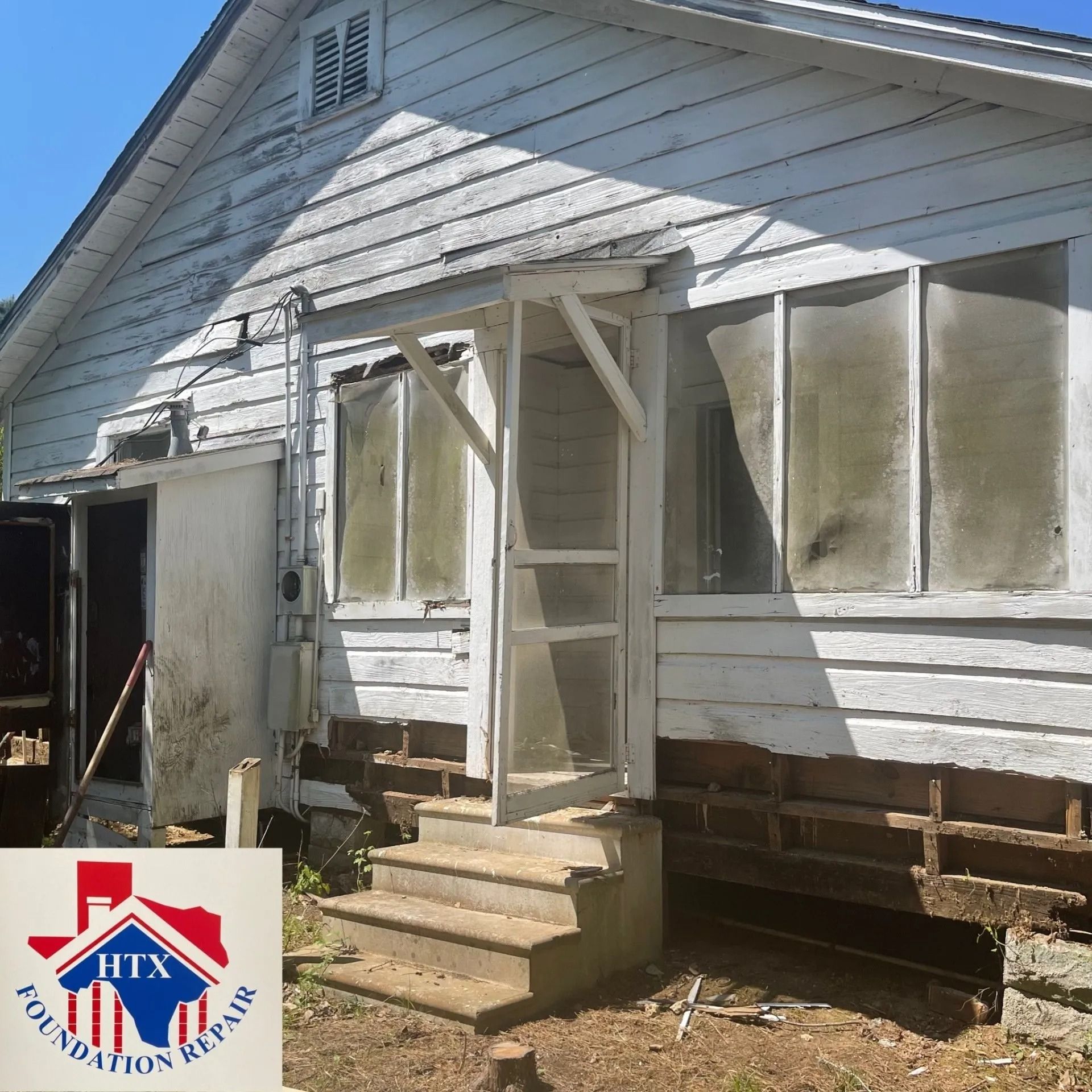 Damaged white house exterior with boarded windows, leaning porch steps, and exposed foundation.