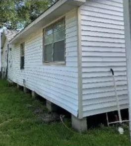 White mobile home with horizontal siding, raised on cinder blocks beside a grassy yard.