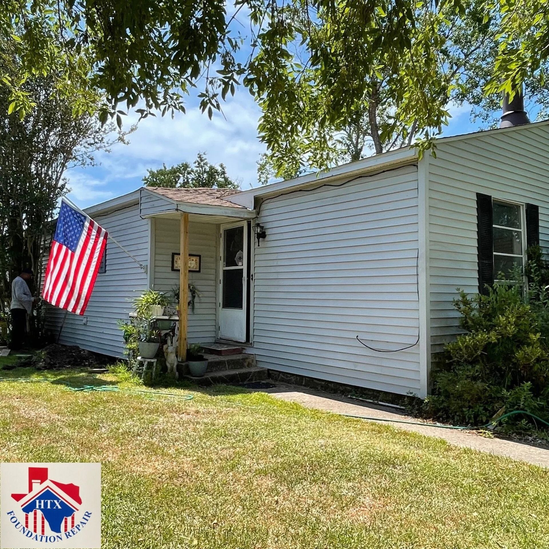 Single-story white house with American flag, front porch, and green lawn under leafy trees
