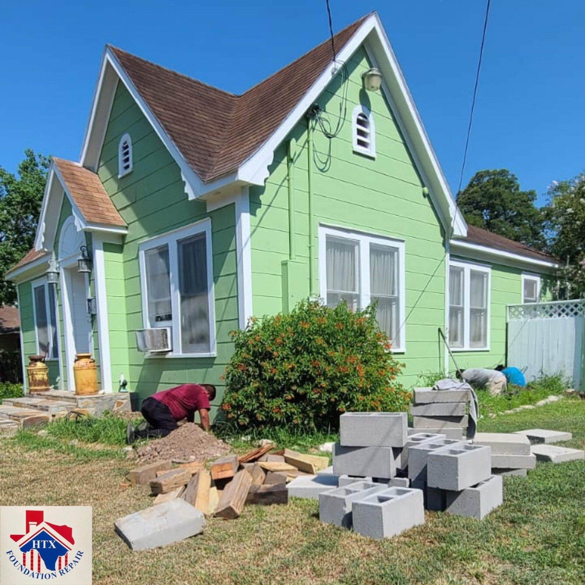 Green house with a steep roof, construction blocks, and a person working in the yard