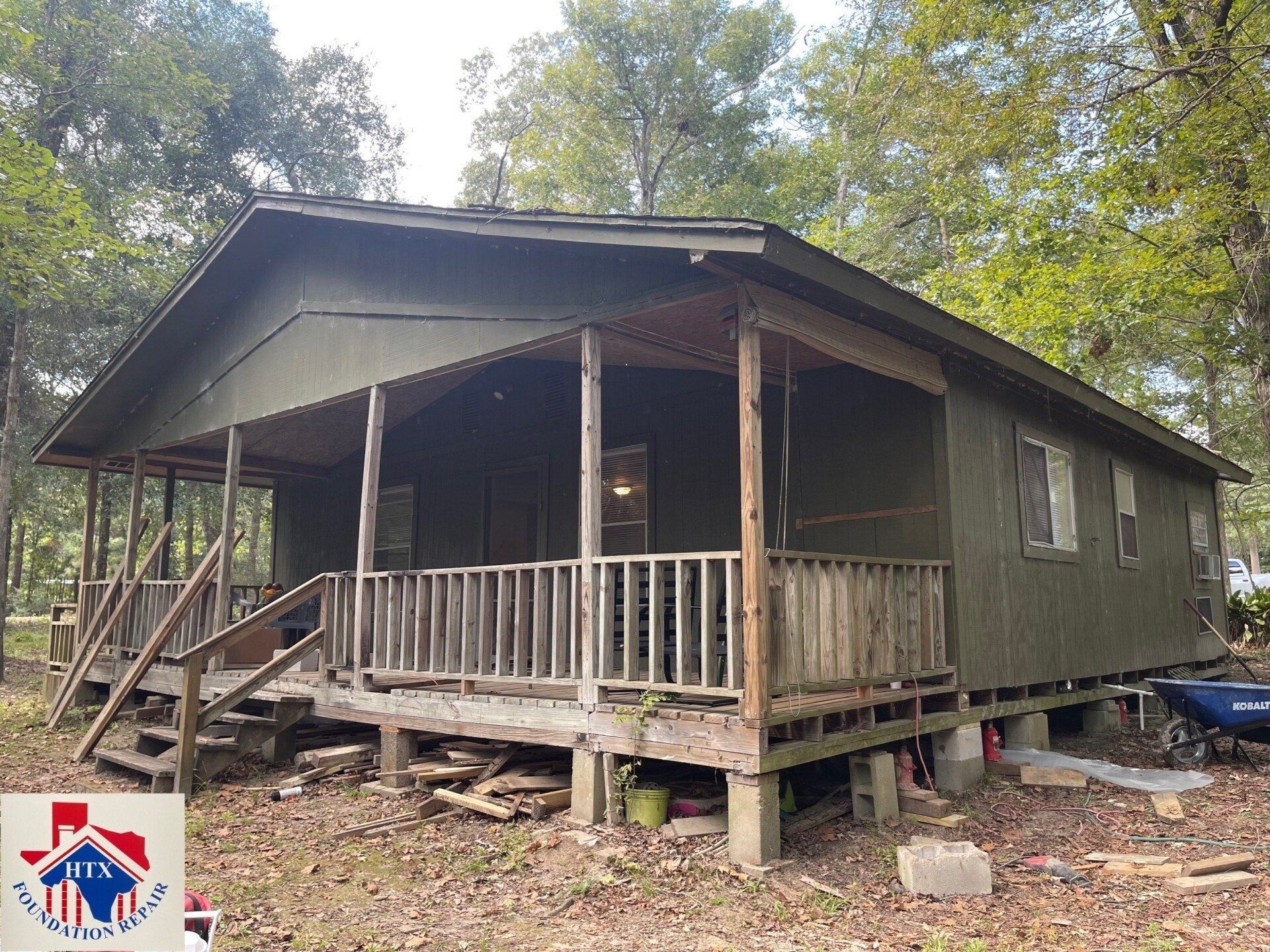 Rustic green cabin with front porch in a wooded area, elevated on posts.