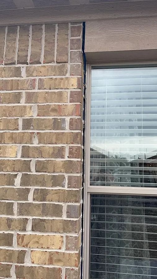 Brick exterior wall beside a window with white blinds and a brown awning above