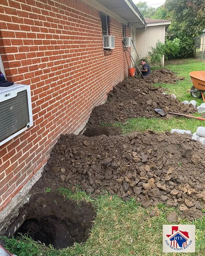 Excavated dirt trench and sinkhole beside a brick house, with piles of soil and a yard air conditioner.