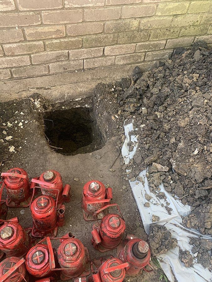 Red fire hydrants clustered beside a brick wall and a dark dug-out hole in the ground