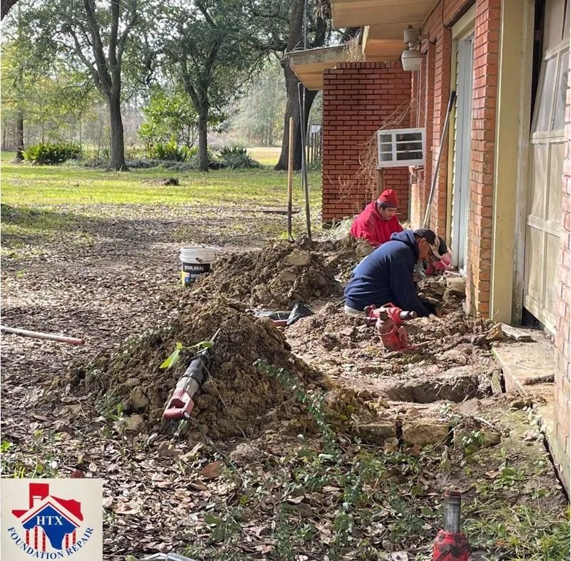 Workers clearing debris beside a brick building, with piles of leaves and tools on the ground.