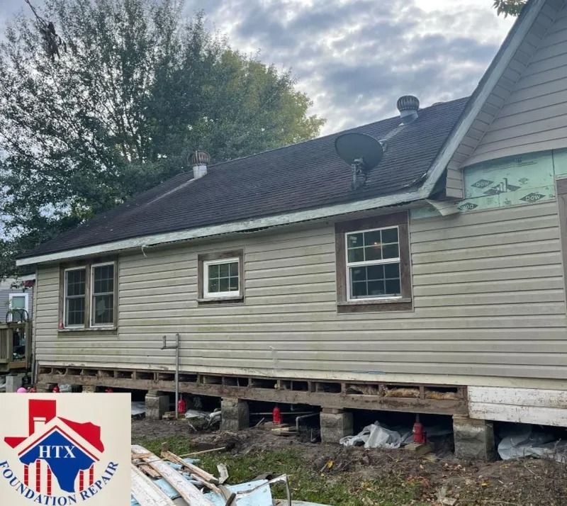 Damaged beige house with missing foundation panels and debris under the raised exterior walls