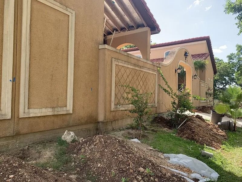 Mounds of dirt and debris beside a beige house with boarded windows and a sloped lawn