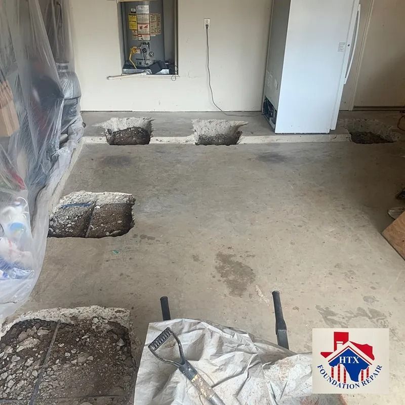 Concrete floor with several square holes in an unfinished room, tools and a white cabinet in the background