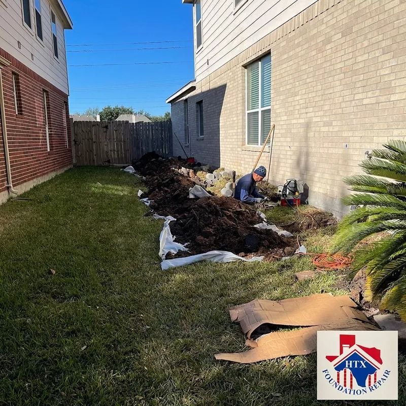 Trash bags and debris lined along a grassy side yard beside a tan building and brick house.