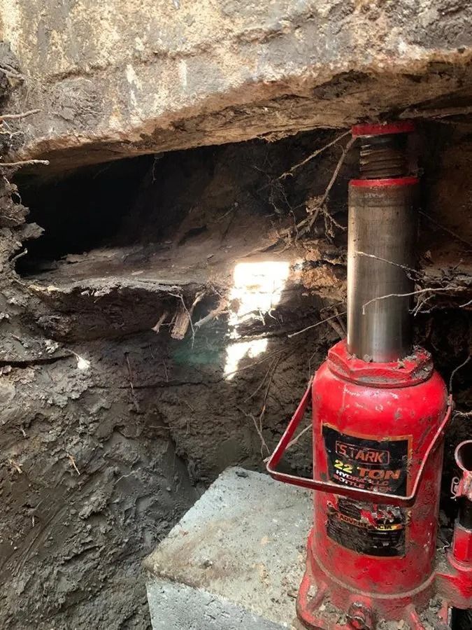 Red hydraulic jack propping up a rock overhang in a narrow cave opening