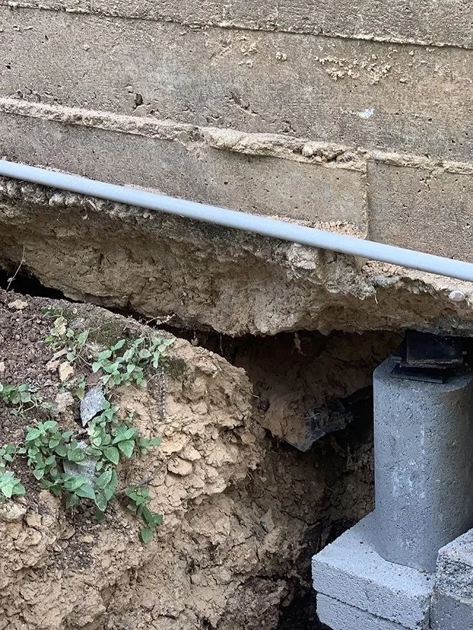 Eroded dirt bank under a concrete slab with a white pipe and exposed foundation support