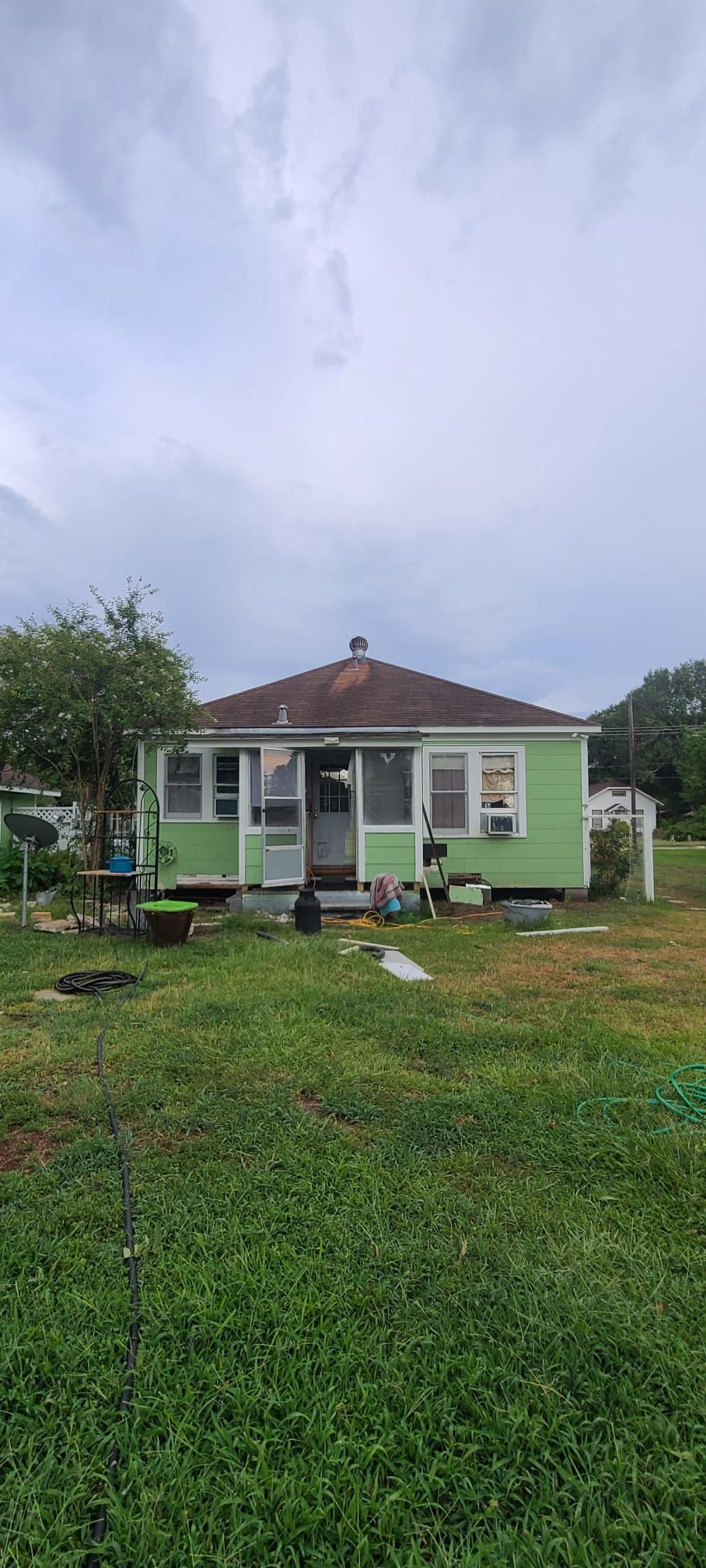Small green house with a red roof in a grassy yard under a cloudy sky