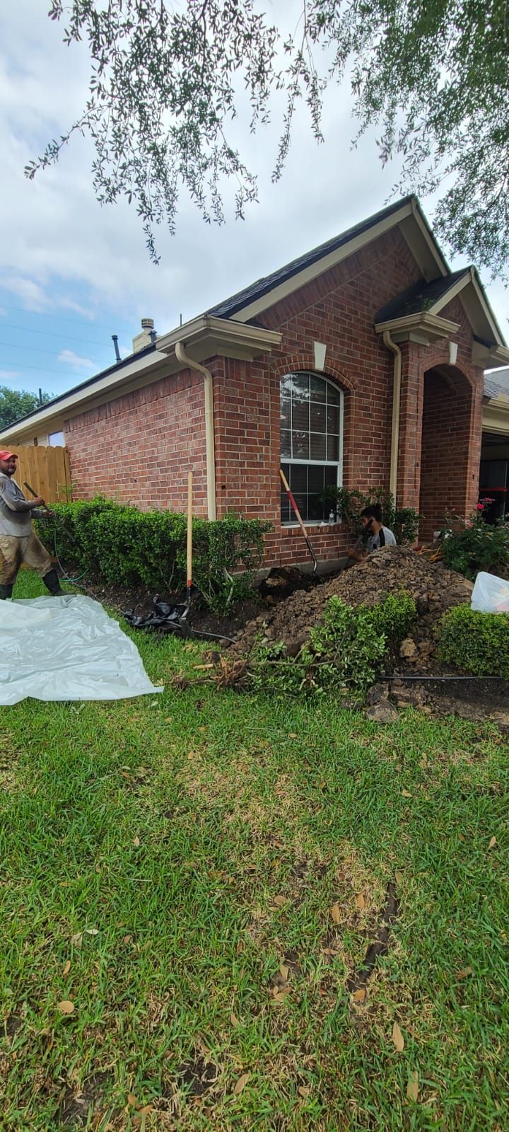 Brick suburban house with a front lawn, shrubs, and a small covered porch under a cloudy sky
