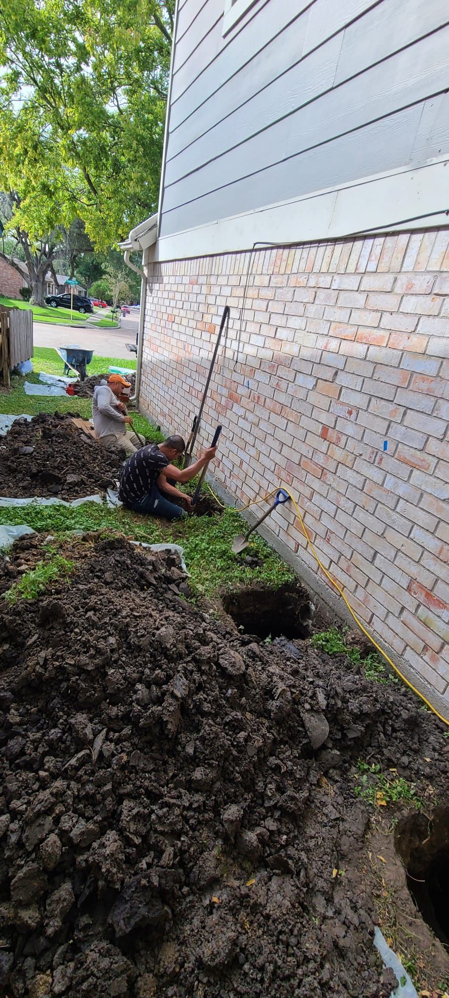 Collapsed dirt pile beside a brick-and-siding house wall with exposed landscaping and green grass.