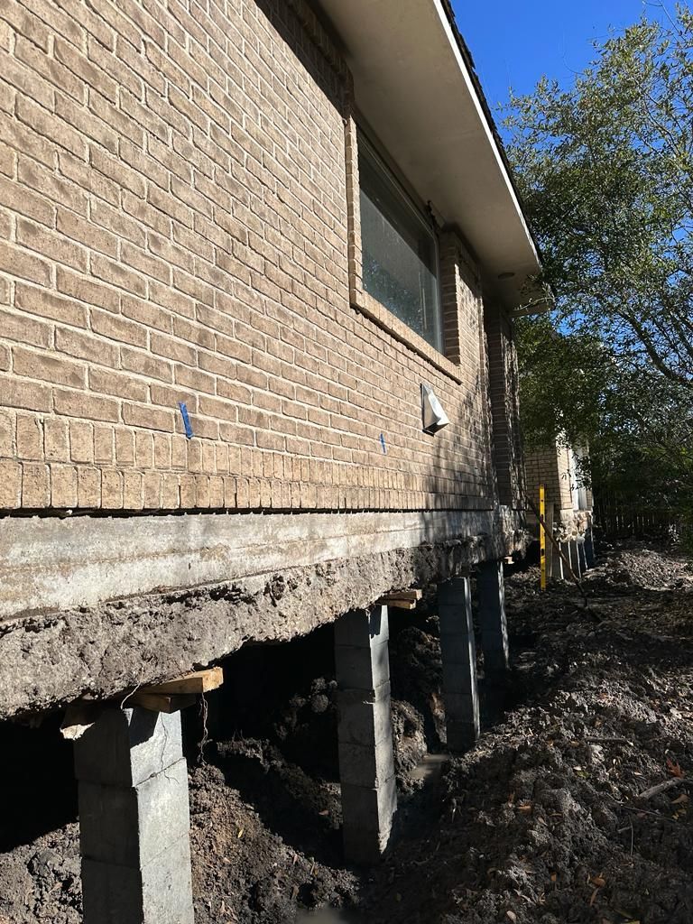 House lifted on temporary supports after foundation excavation, with exposed crawlspace and dirt trench