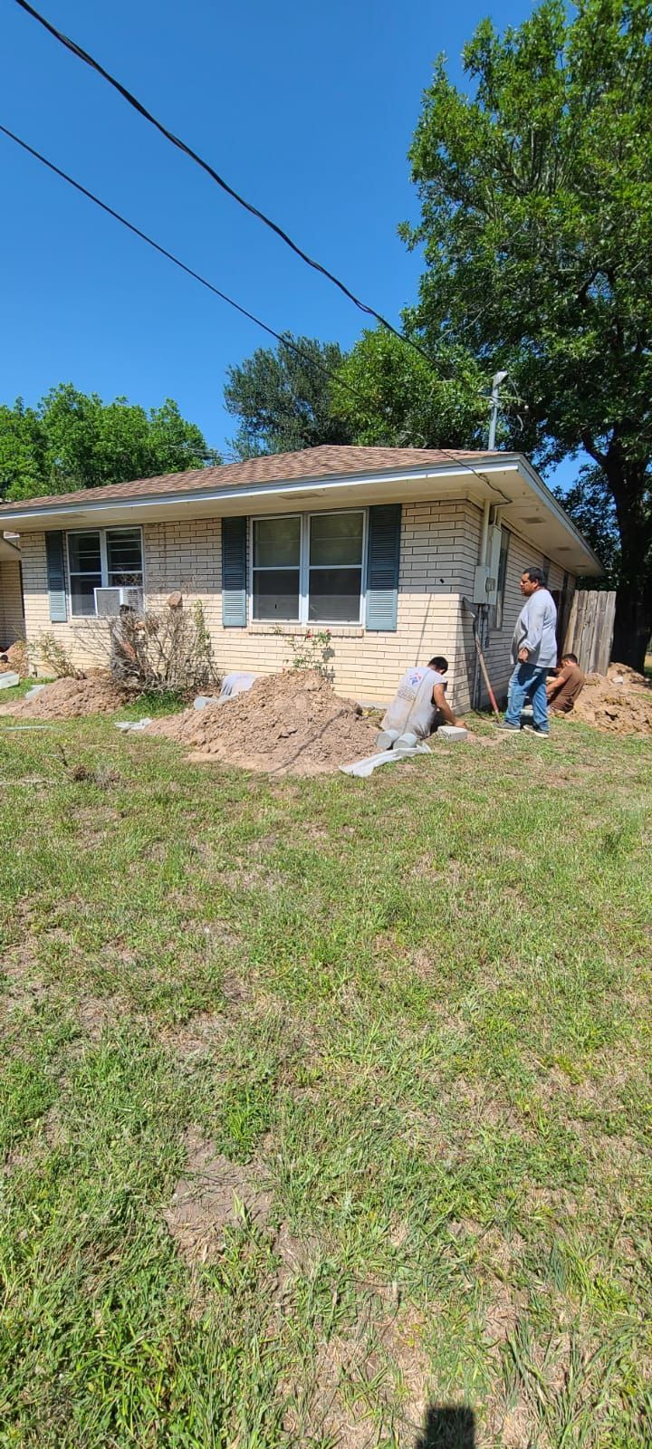 Two people working outside a small house with a pile of debris in the yard on a sunny day
