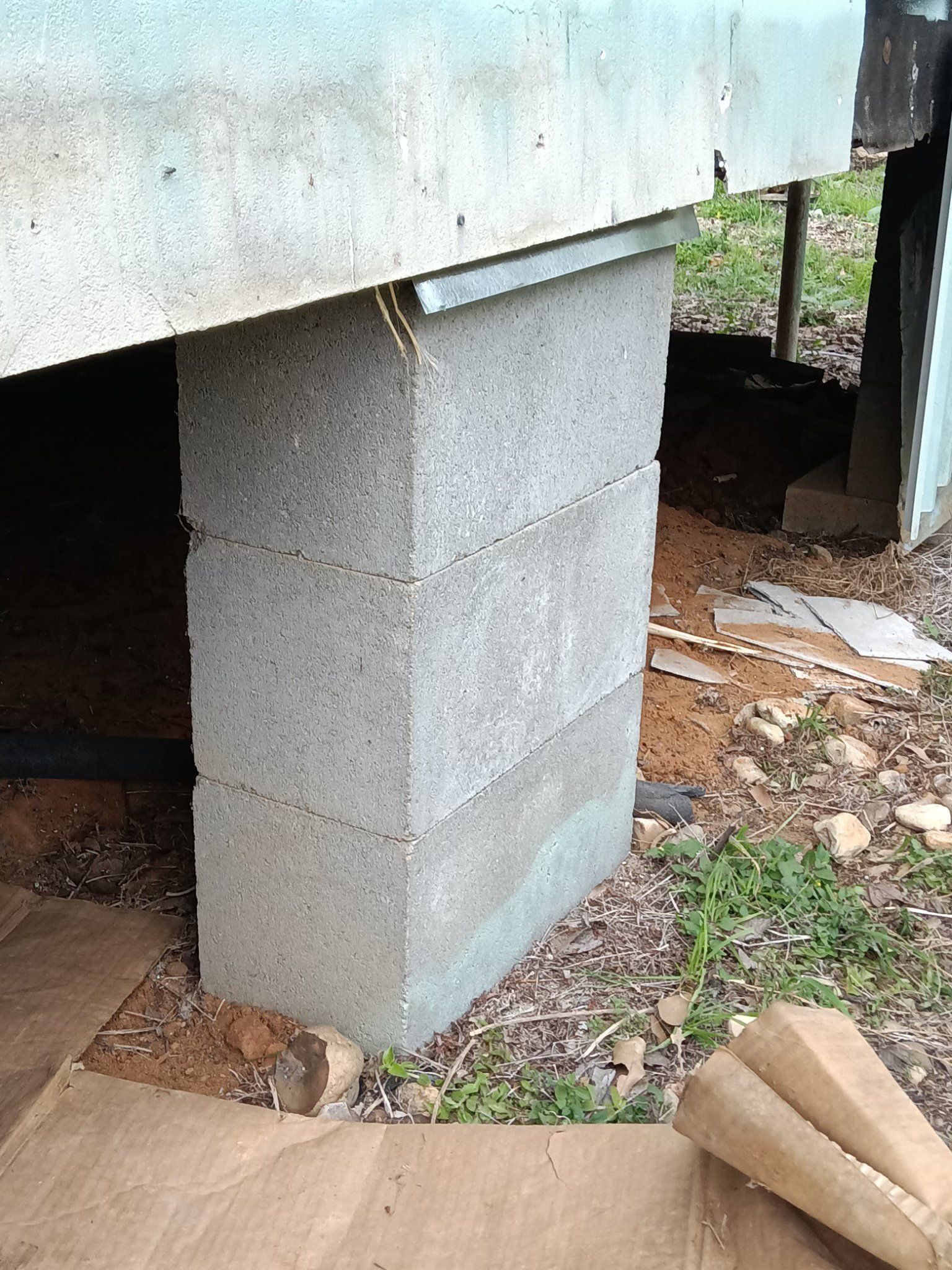 Concrete block foundation supporting a raised structure, with dirt and debris underneath.