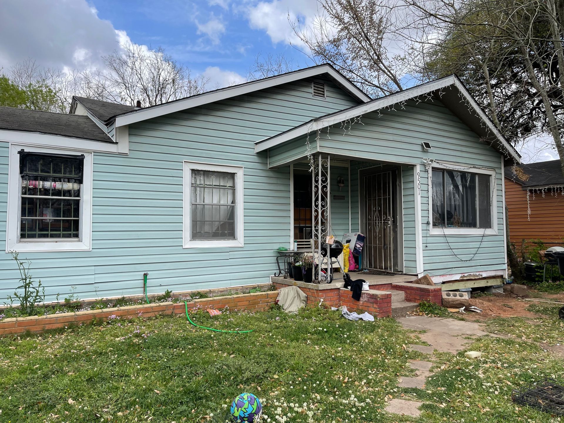 Light blue bungalow with a front porch, windows, and a stone path in a grassy yard under a cloudy sky