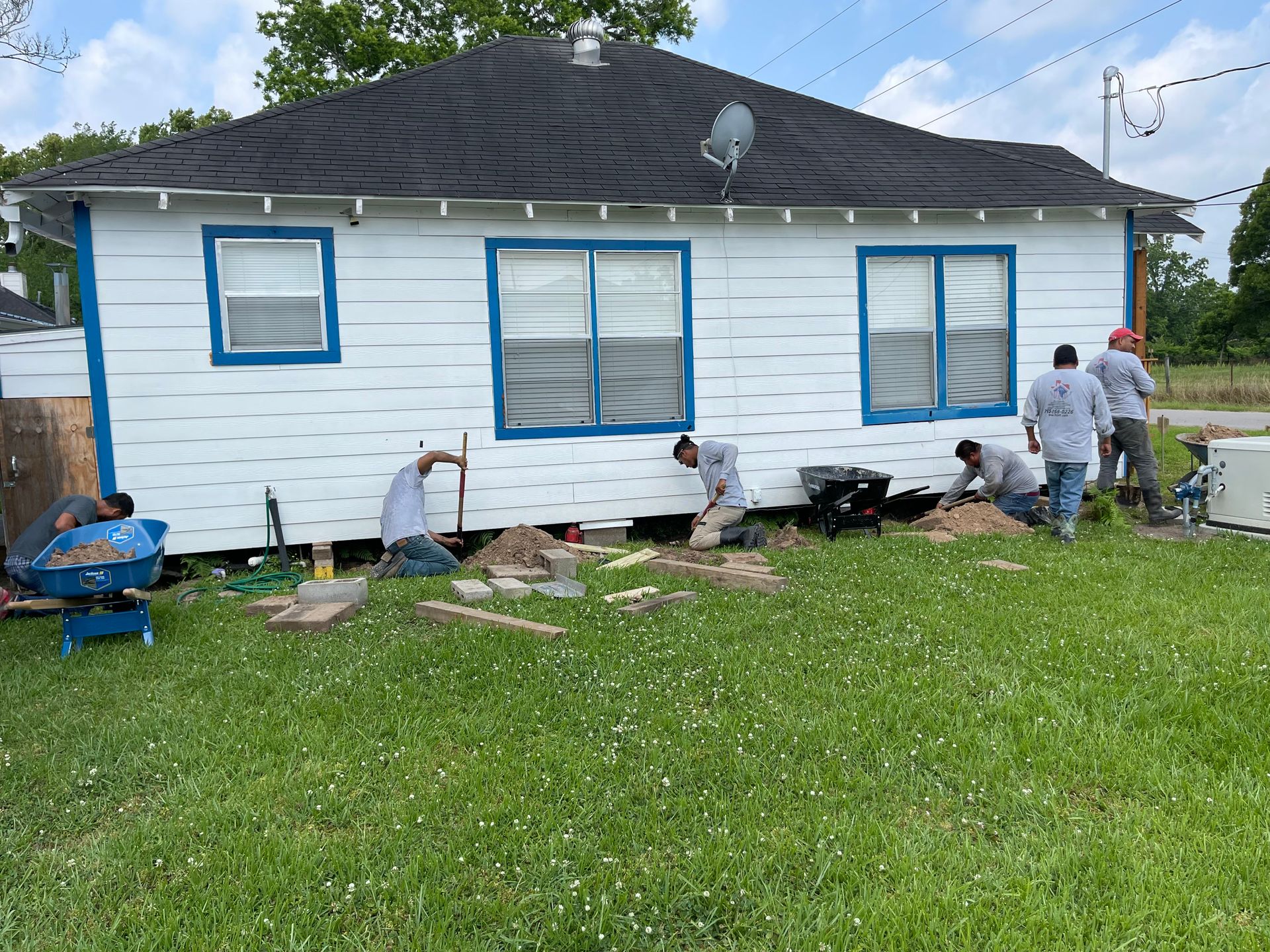 Workers repairing the exterior of a white house with blue-trimmed windows and green lawn