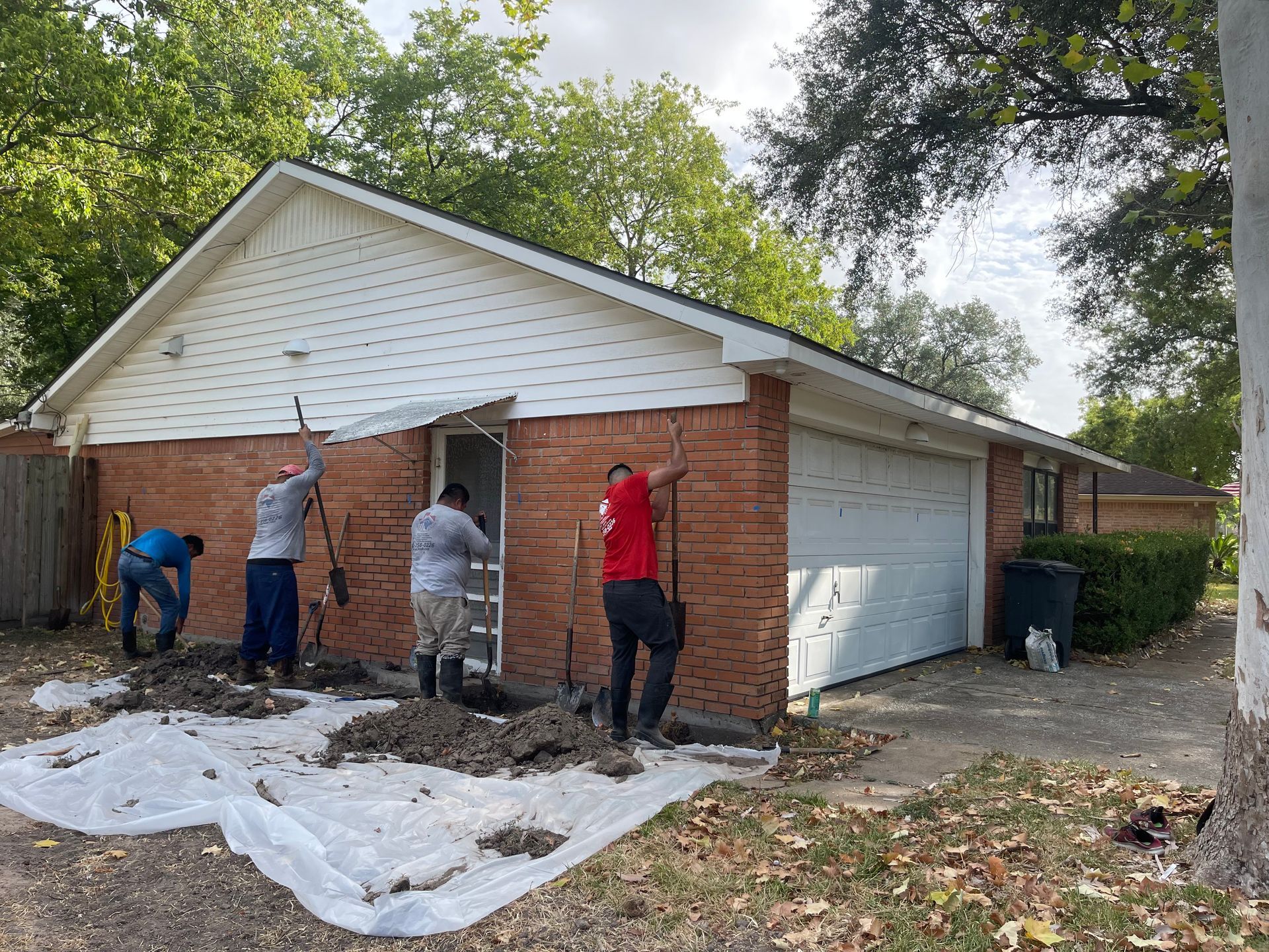 Workers repair the brick exterior of a single-story house with white siding and a garage.