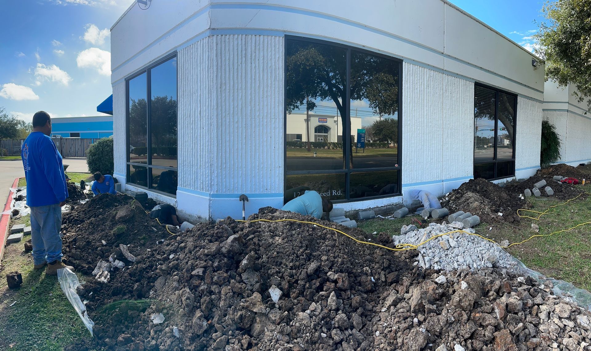 Worker beside dirt pile outside curved glass building under construction