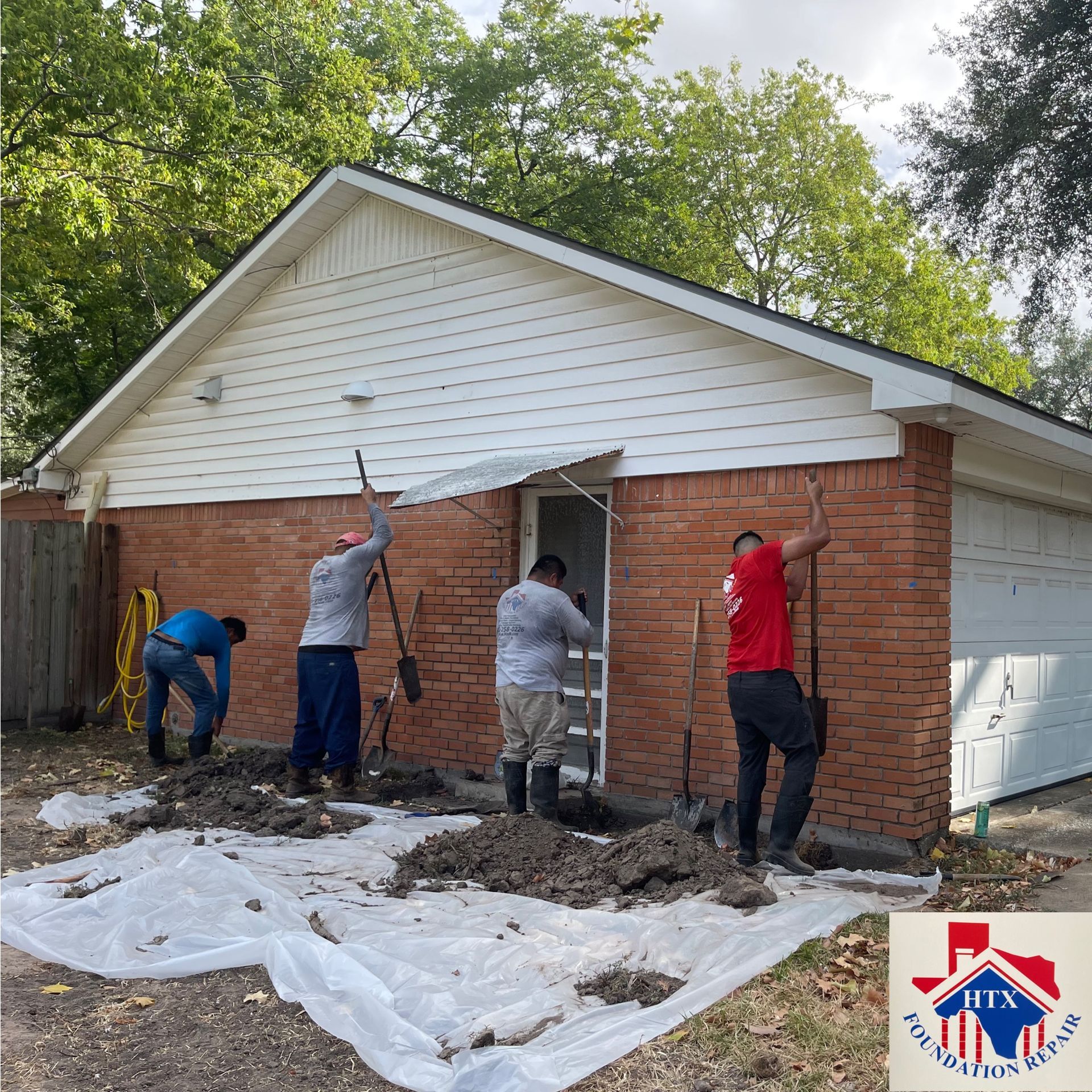 Four workers repair a brick garage wall with tools and tarps in a backyard